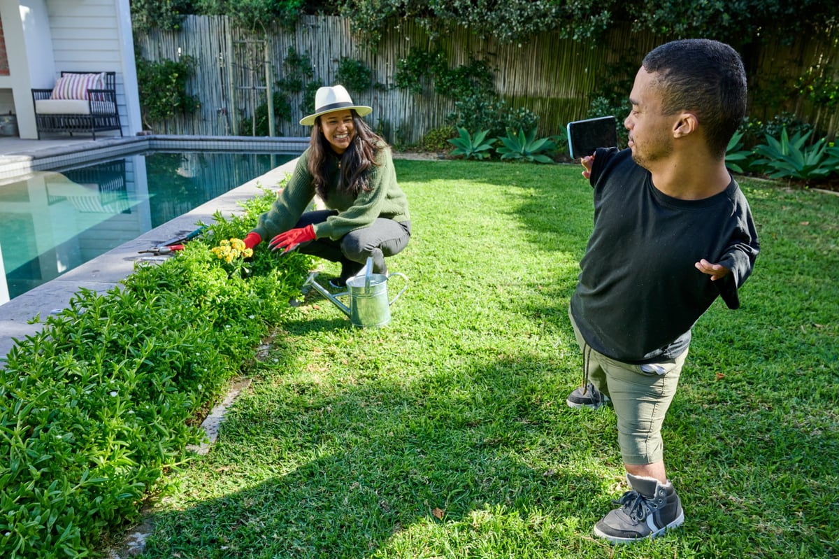 Man with phocomelia photographing smiling woman gardening