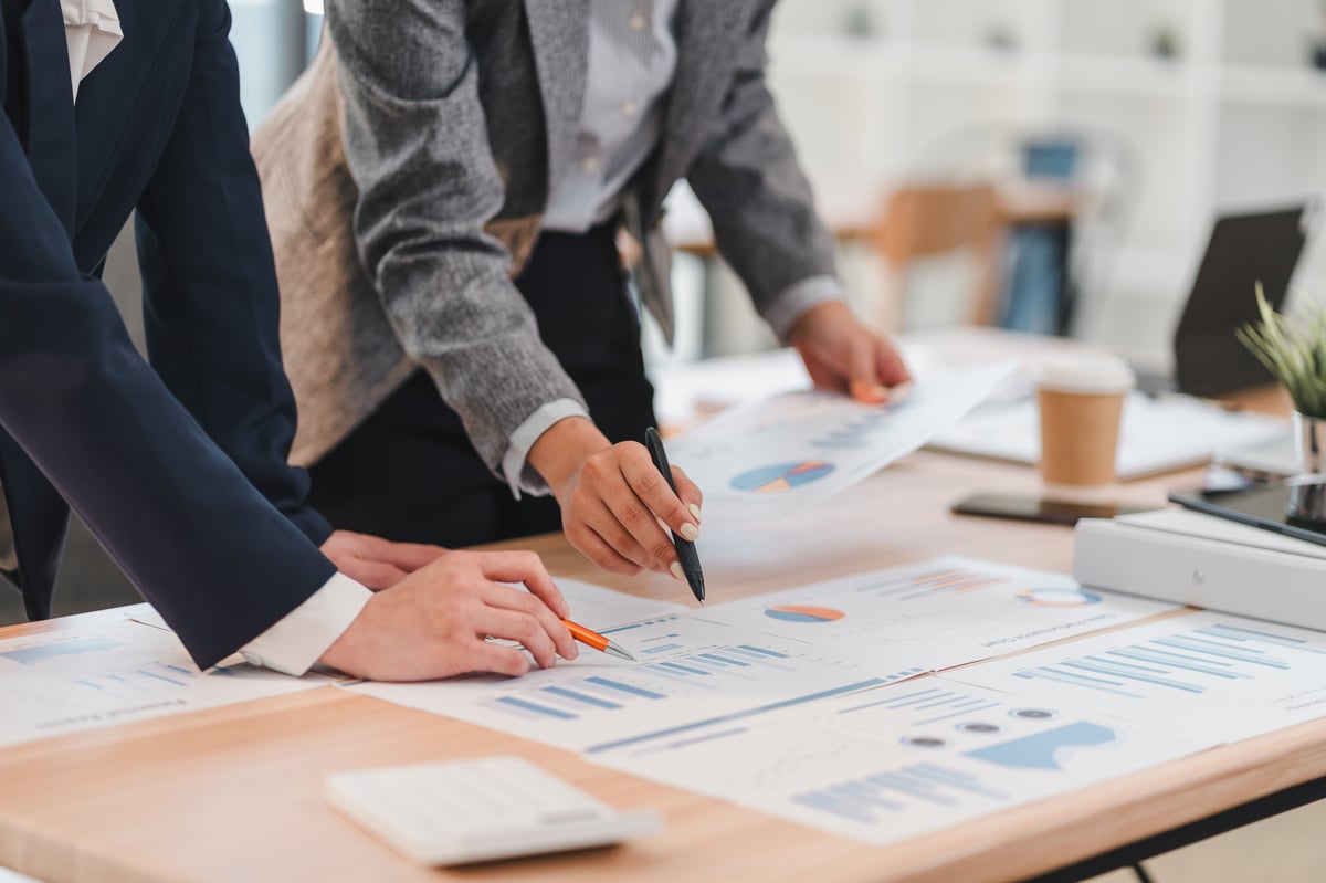 Two business professionals analyzing financial charts and graphs on wooden desk in modern office setting.