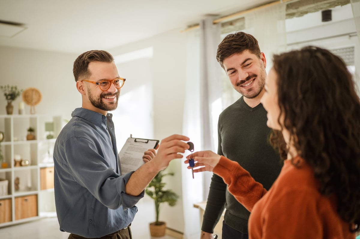 Real estate agent smiling while handing over new house keys to a happy young couple.